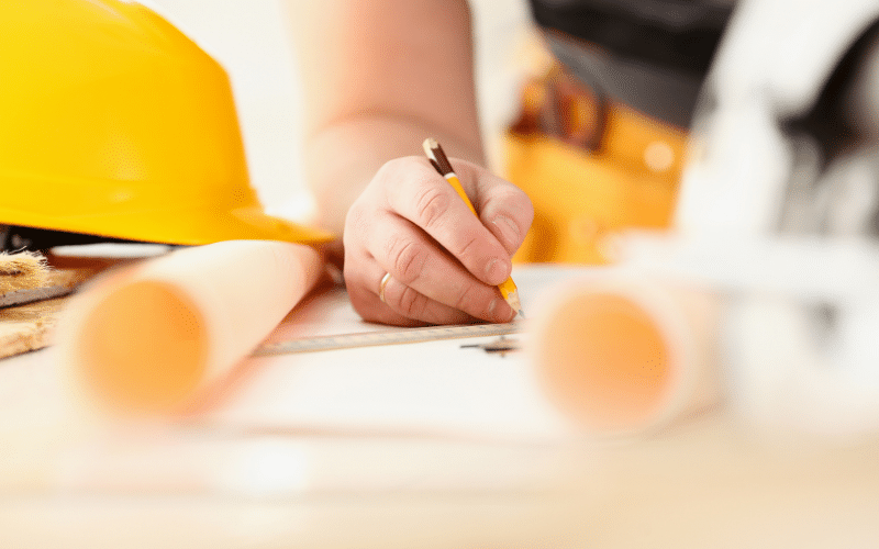 Main d’un professionnel du bâtiment travaillant sur un plan, symbolisant la préparation des contenus d’un site web pour artisan.