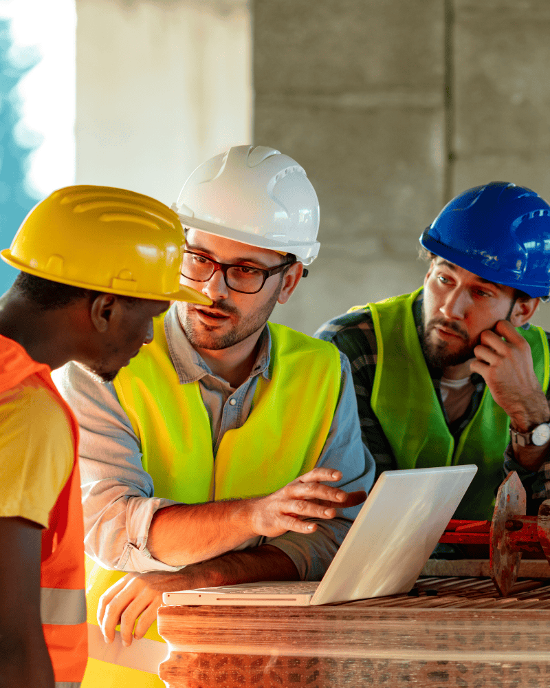 Artisans du bâtiment collaborant autour d’un ordinateur sur un chantier pour illustrer le suivi et l’amélioration continue d’un site web artisan.